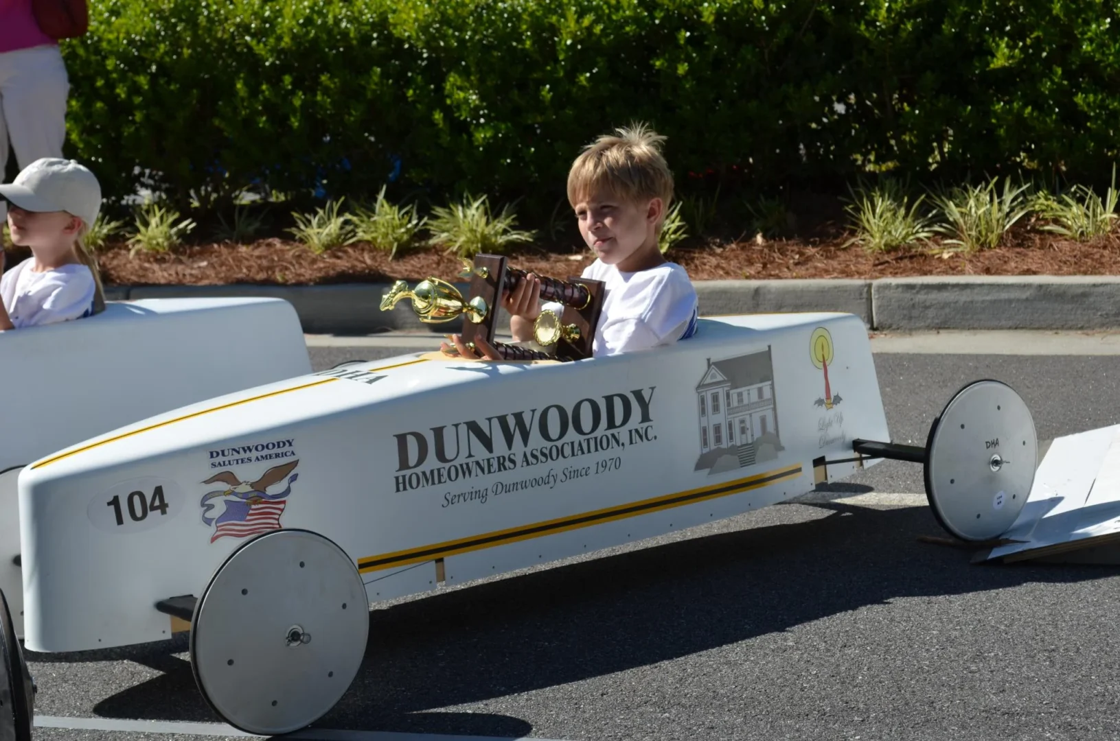 Boy with trophy in soap box car with Dunwoody Homeowners Association's logo on side